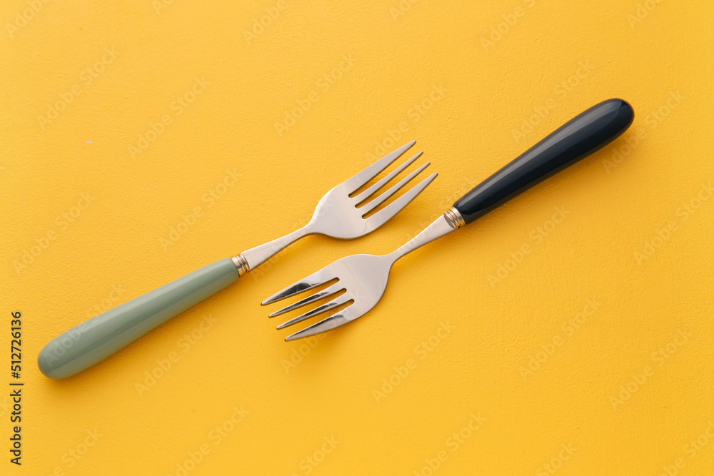 Stylish stainless steel forks on yellow background