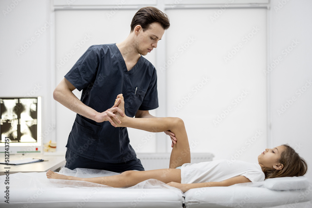 Pediatric orthopedist examines limbs and joints of 10-aged girl on couch in the medical office. Conc