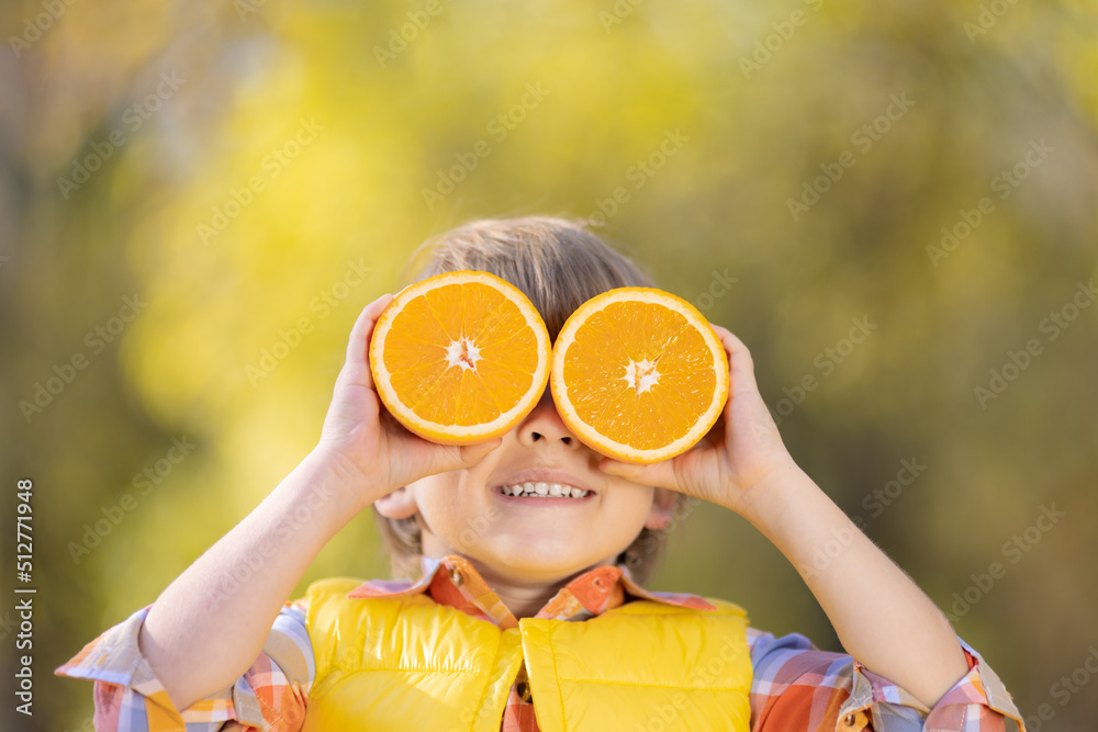 Surprised child holding slices of orange in autumn park