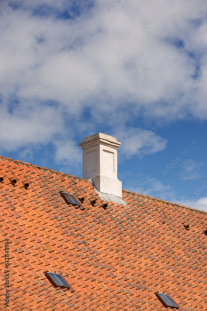 Chimney designed on slate roof of house building outside against blue sky with white clouds backgrou