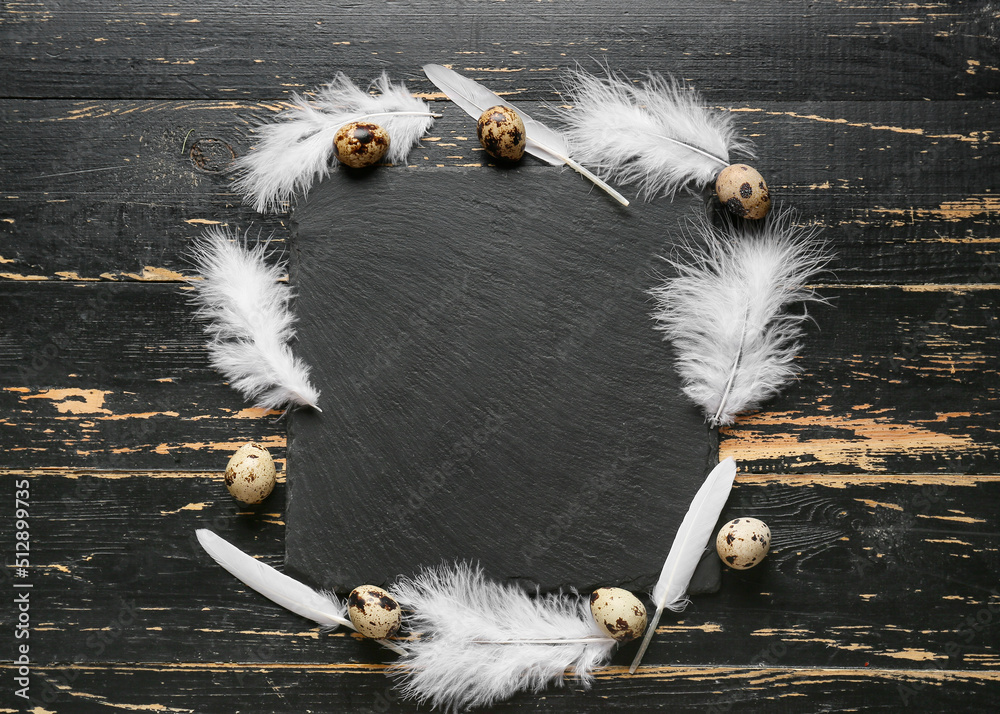 Composition with beautiful white feathers, quail eggs and board on black wooden background