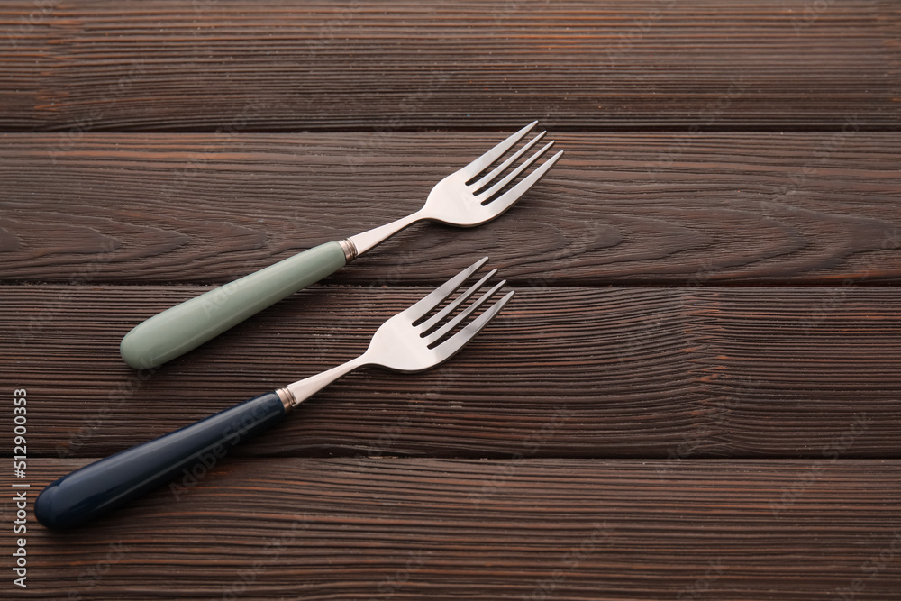 Stylish stainless steel forks on dark wooden background