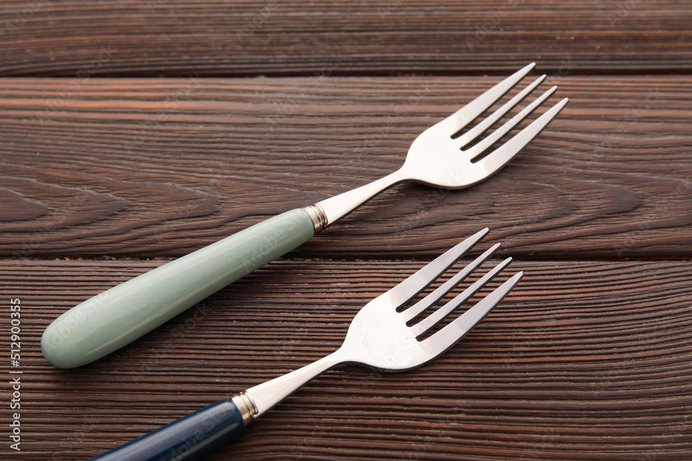 Stylish stainless steel forks on dark wooden background