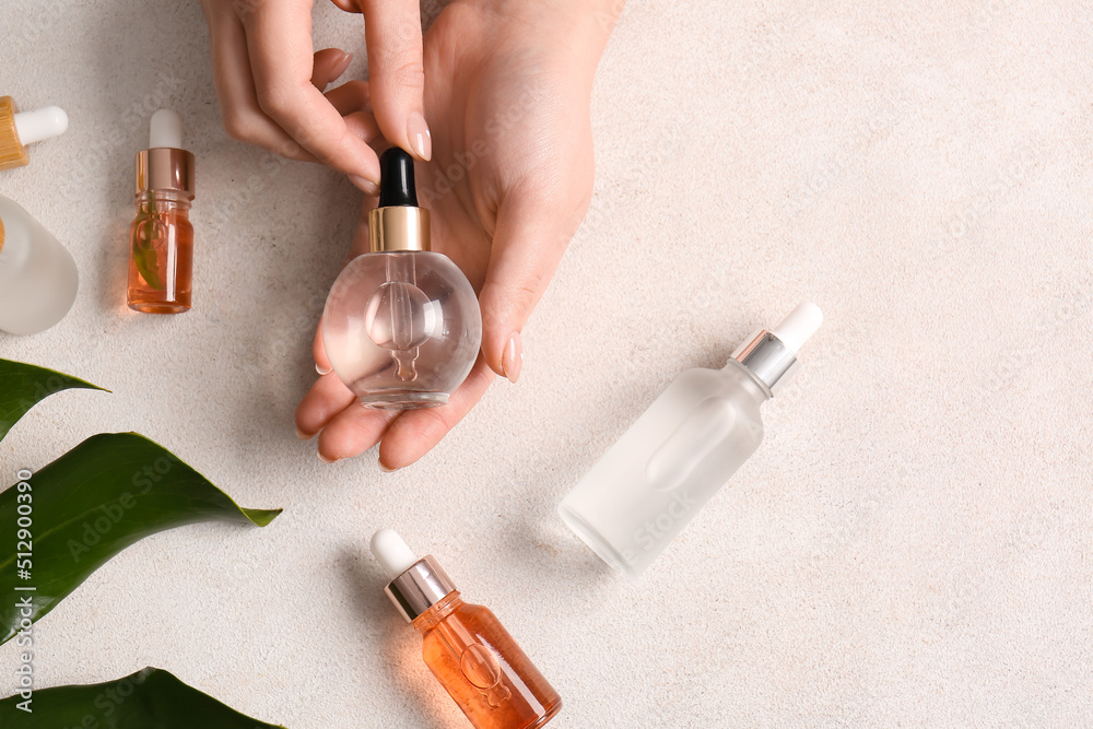 Female hands with different bottles of natural serum on light background