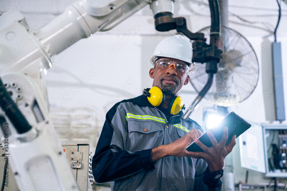 African American factory worker working with adept robotic arm in a workshop . Industry robot progra