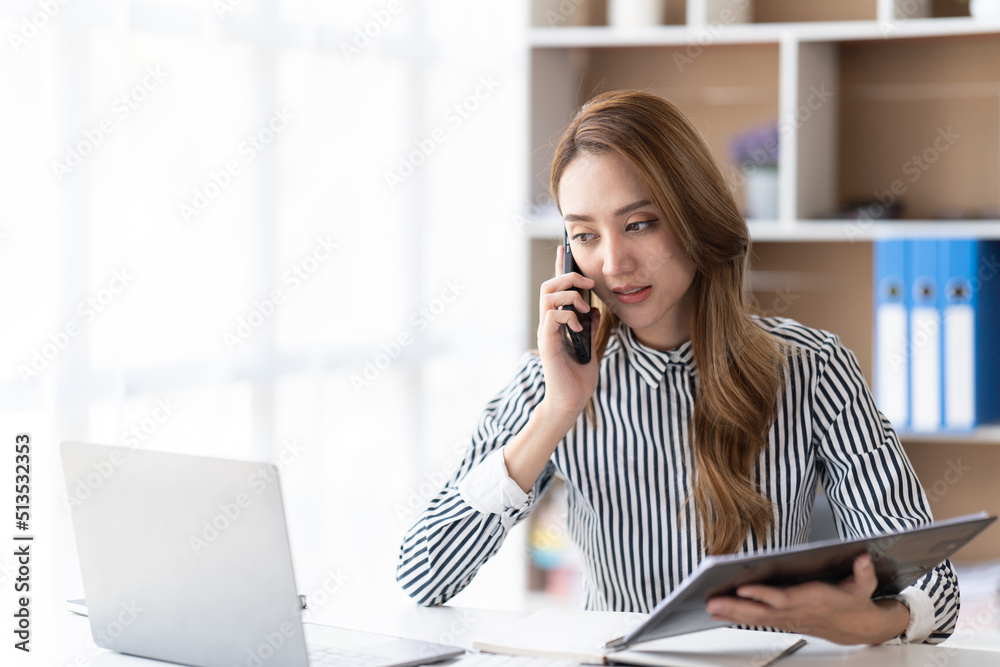 年轻的职场女性在办公室打电话。职场女性在电话里发短信，在lapt上工作