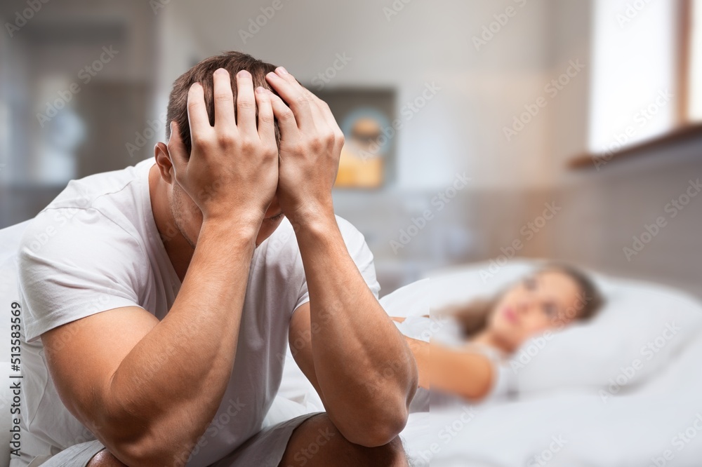 Upset young man in pajamas waking up with headache, lying in bed early in morning, touching his head