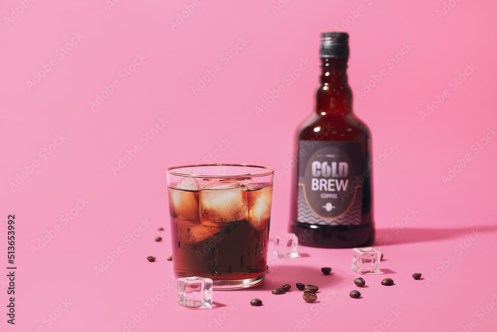 Bottle, glass of cold brew and coffee beans on pink background