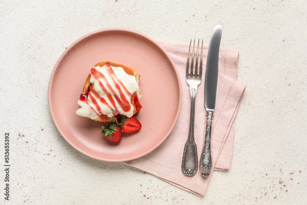 Plate with strawberry cinnamon roll, cutlery and napkin on white background