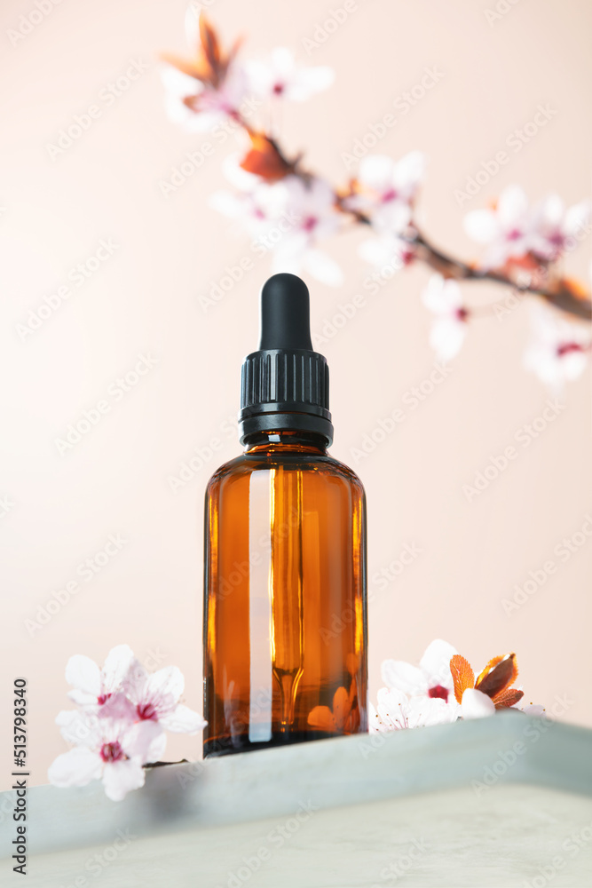 Amber glass dropper bottle and spring cherry blossom flower on marble shelf.  Skincare products , na