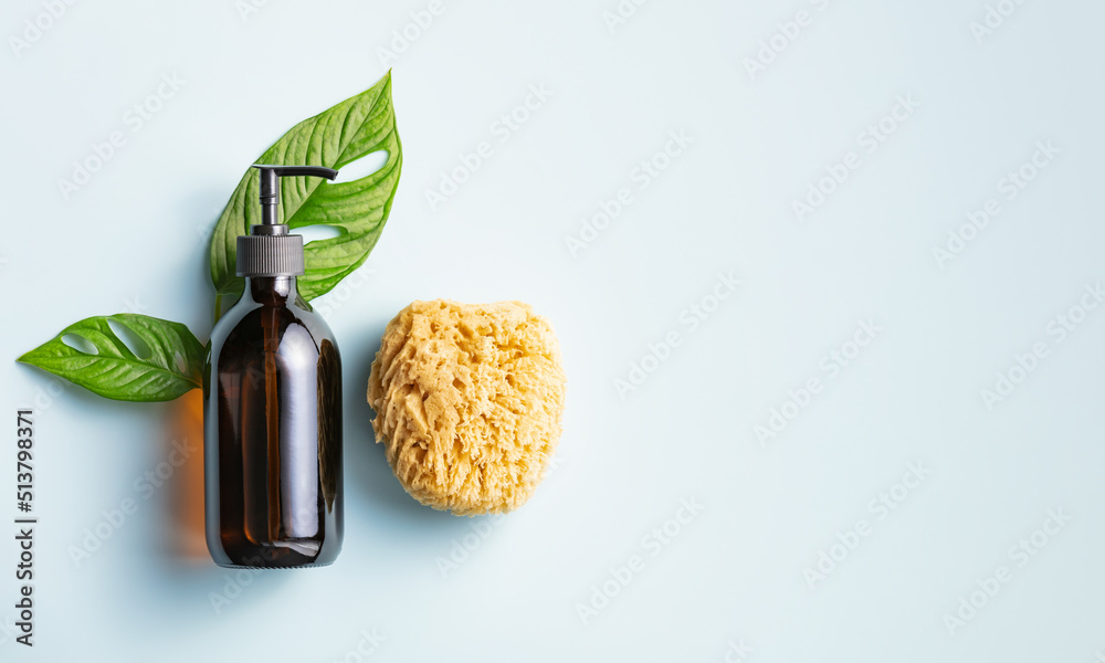 One cosmetic dark amber glass bottle with green plant and loofah on blue background