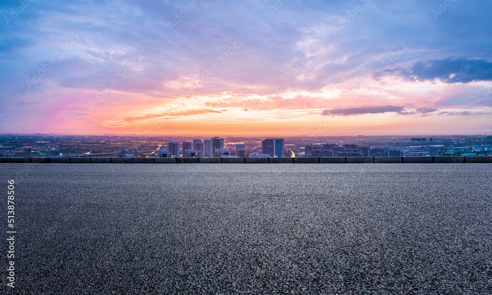 空旷的柏油路和现代化的城市天际线，日落时的建筑景色。高角度视野。