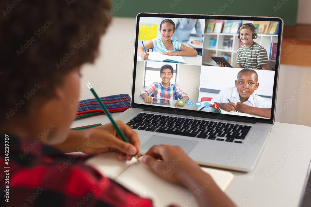 African american girl with afro hair writing in book while learning in online class over laptop