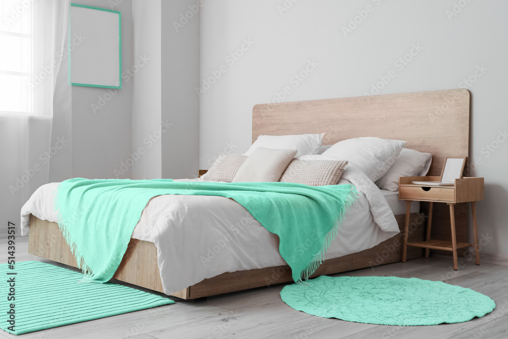 Comfortable bed with mint blanket and rugs in room