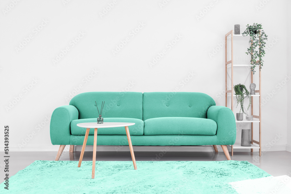 Stylish mint sofa with table and rack near light wall in room