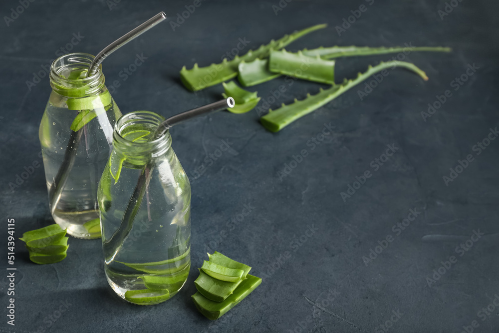 Glass bottles of aloe juice with straws on dark background