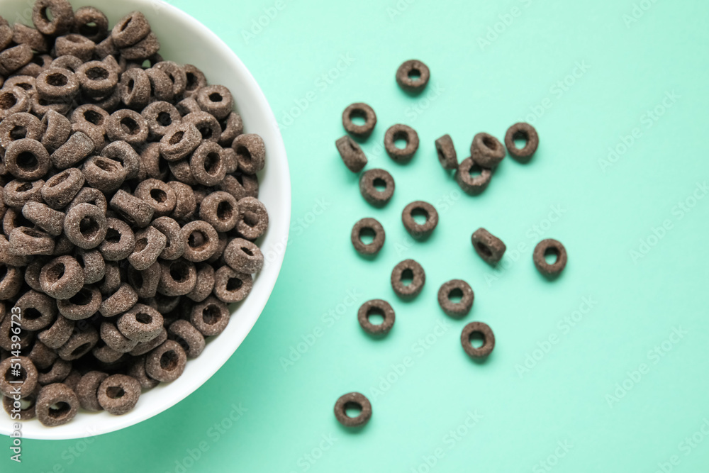 Bowl of black cereal rings on color background, closeup