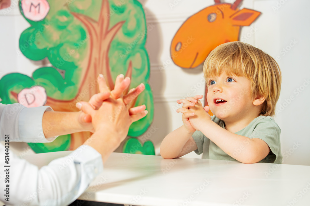 Cute blond boy play finger game sitting by the desk in class