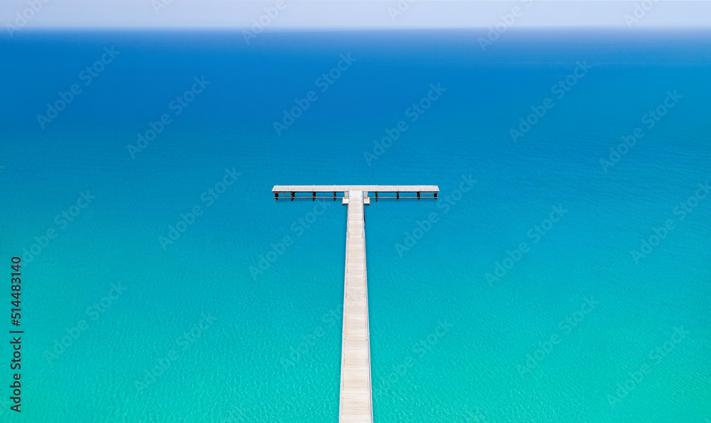 White wooden pier out to calm blue sea, minimal landscape. Drone view from above