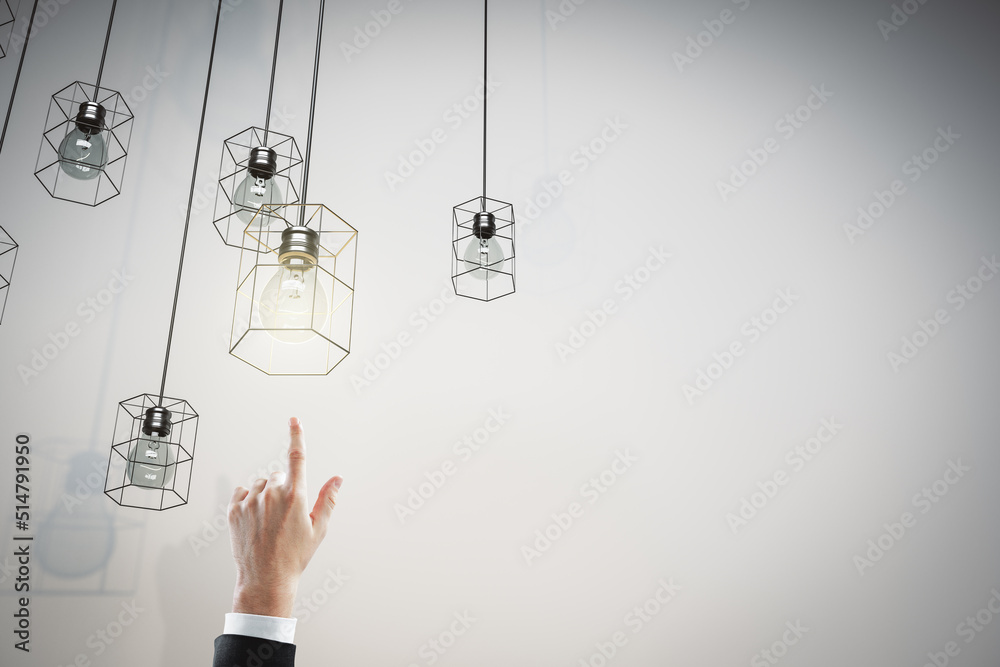 Close up of businessman hand pointing at creative lamps hanging on concrete wall background with moc