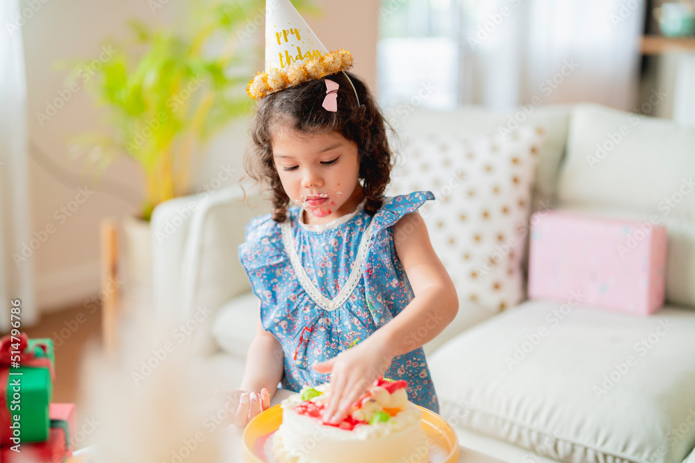 生日快乐，穿着周年纪念服，戴着派对帽的小女儿为h享用手指美味的甜蛋糕