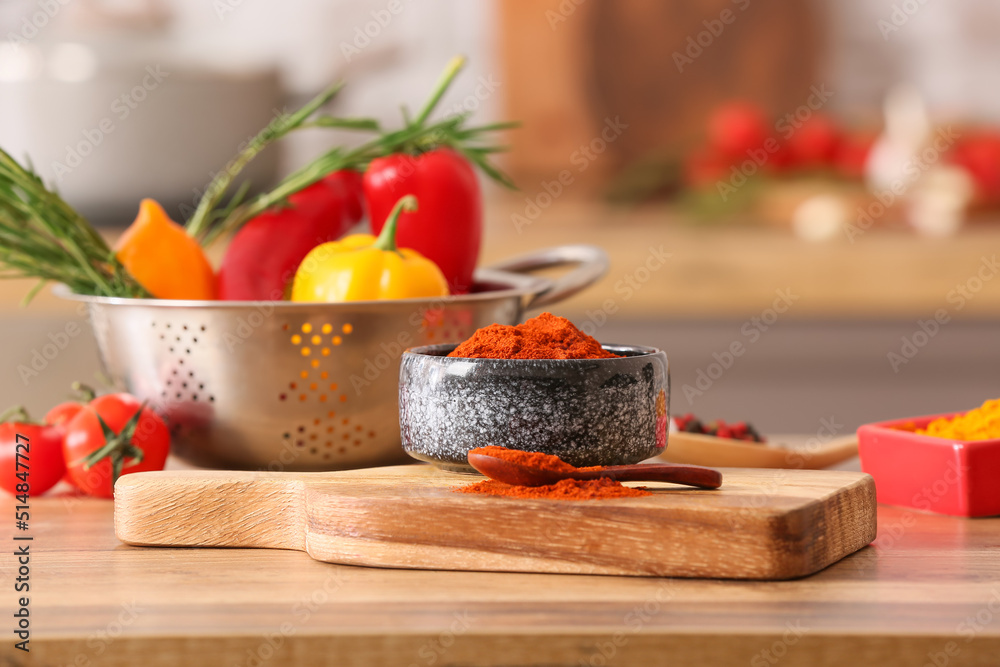 Wooden board with bowl of paprika powder on table in kitchen