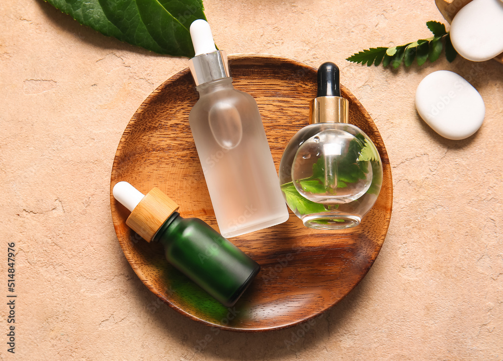 Wooden plate with bottles of natural serum on color background