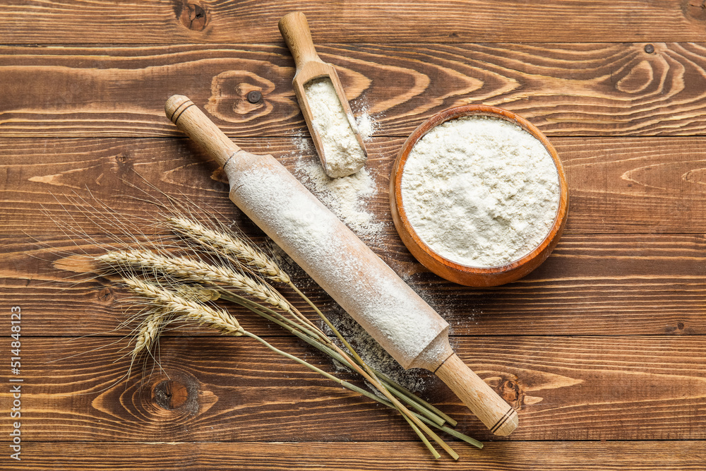 Wheat ears, rolling pin, scoop and bowl with flour on wooden background