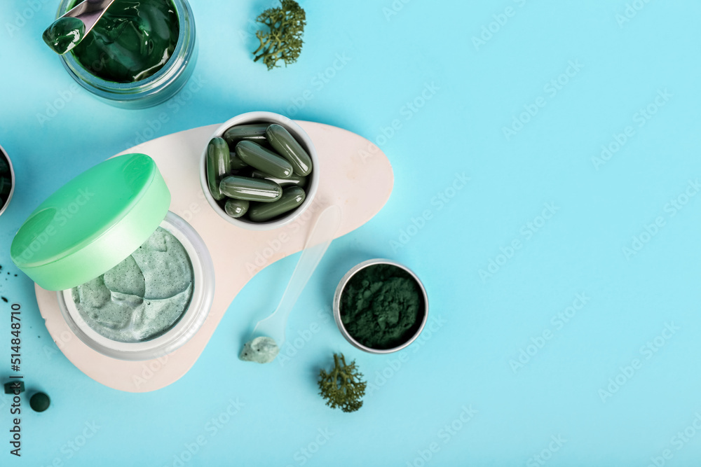 Composition with jars of spirulina facial mask, powder and pills on blue background