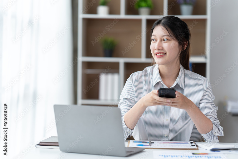 Asian businesswoman in formal suit in office happy and cheerful during using smartphone and working.