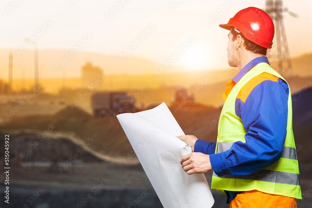 A young mine worker wearing protective wear with coal mine in the background