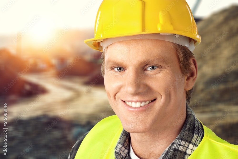 A young mine worker wearing protective wear at the camera with coal mine in the background