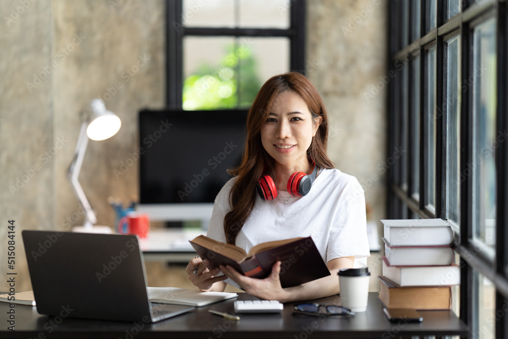 一名年轻的女学生坐在桌子旁，学习时使用电脑笔记本电脑。