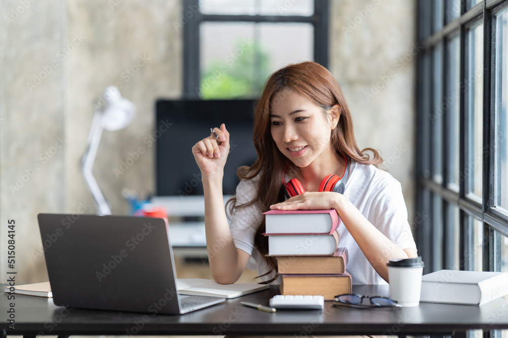 一名年轻的女学生坐在桌子旁，学习时使用电脑笔记本电脑。