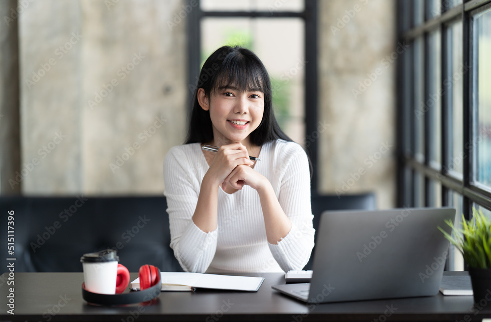 一名年轻的女学生坐在桌子旁，学习时使用电脑笔记本电脑。