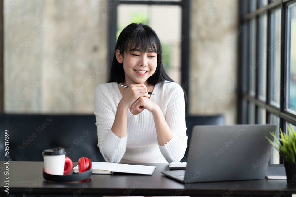 一名年轻的女学生坐在桌子旁，学习时使用电脑笔记本电脑。