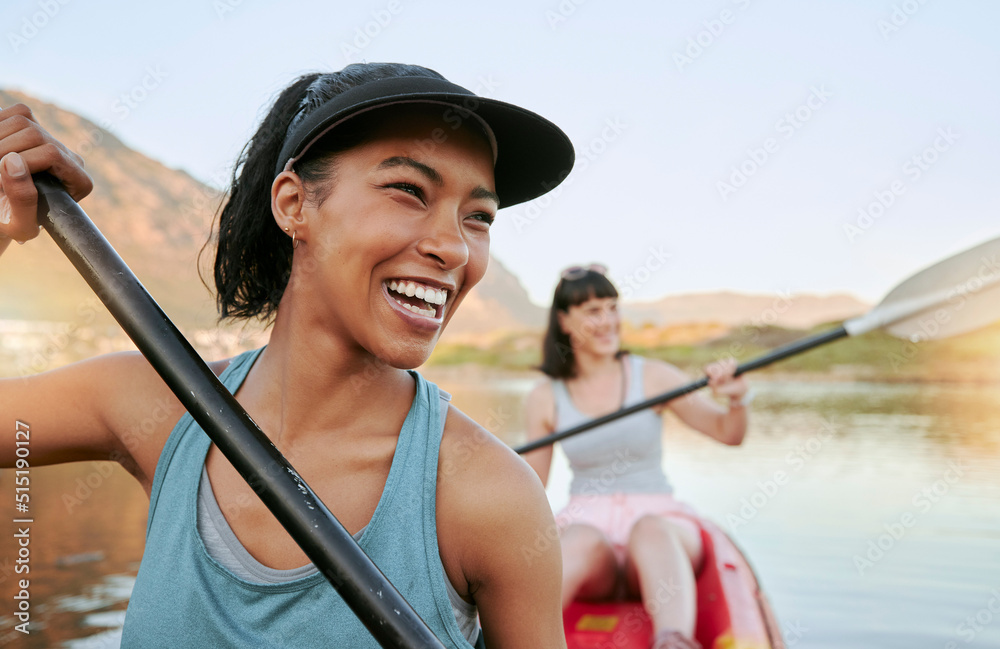 Two smiling friends kayaking on a lake together during summer break. Smiling and happy playful women