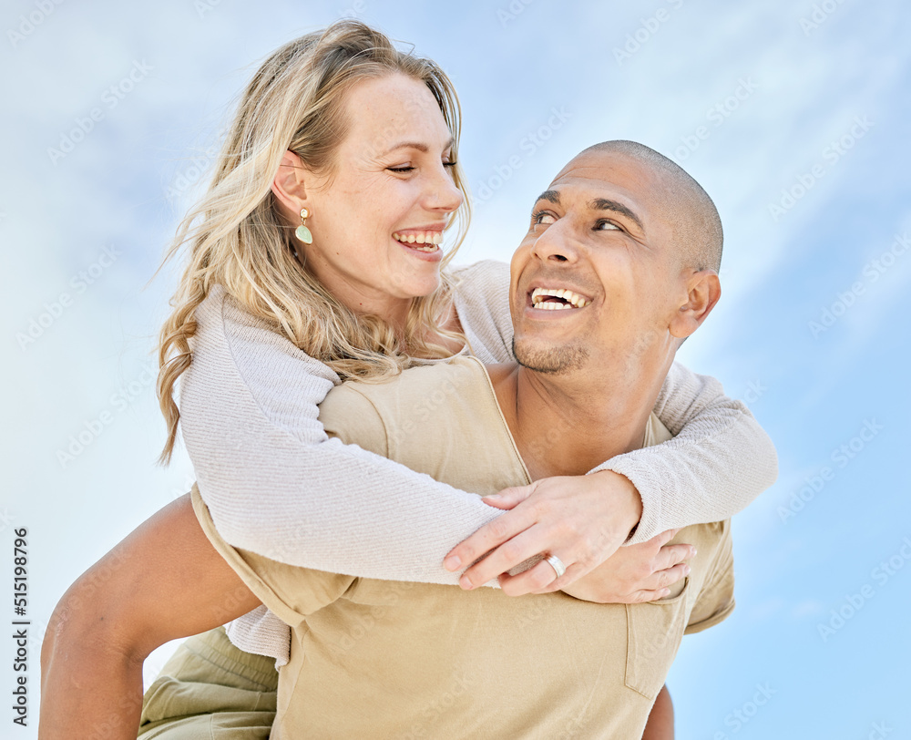 Happy interracial couple enjoying a piggyback ride outside against a blue sky having fun and smiling