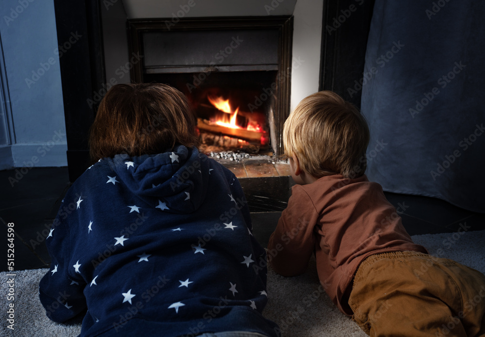 Two boys lay in front of the home fireplace look at fire