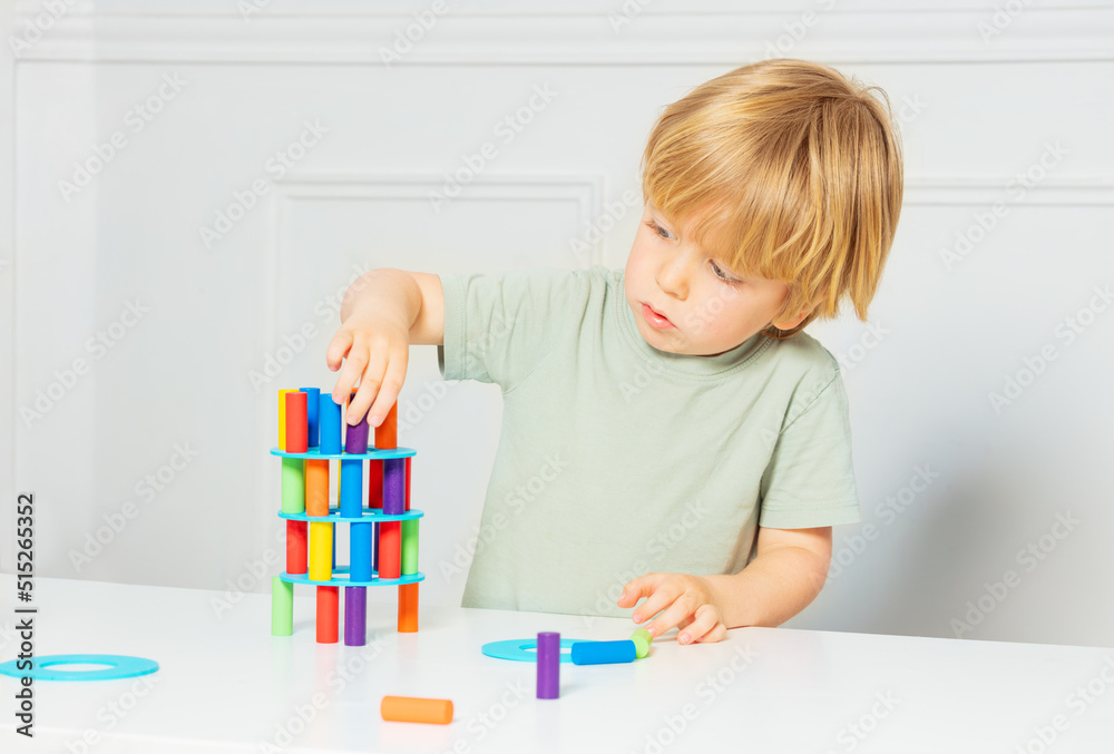 Concentrated boy constructs tower of color blocks on the table