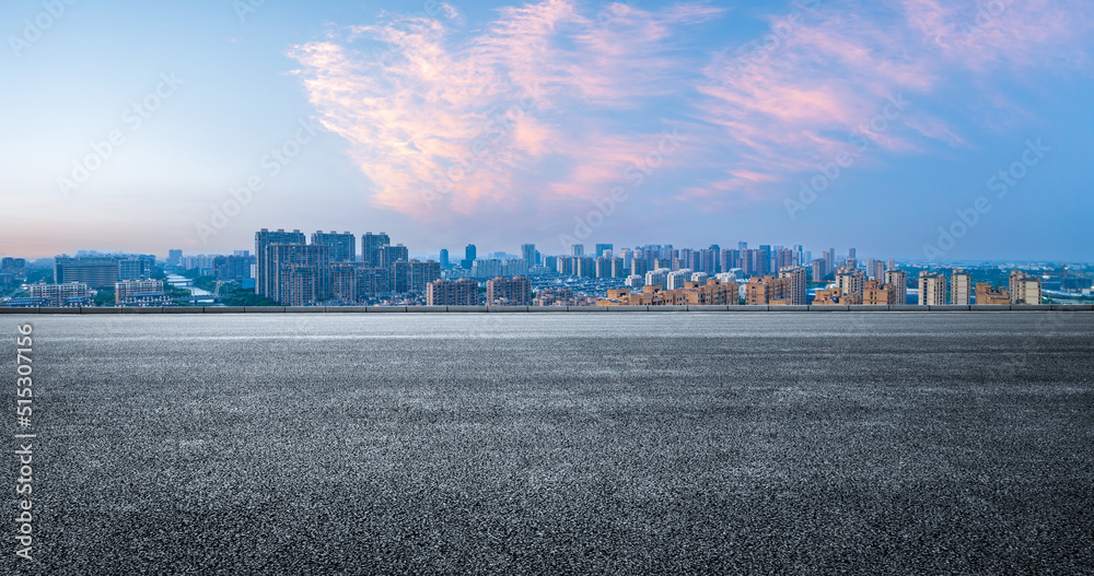 空旷的柏油路和现代化的城市天际线，日落时的建筑风光