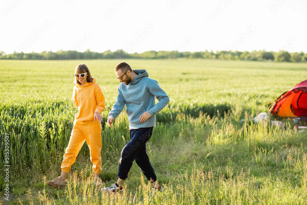 这对年轻夫妇在夏天带着帐篷在绿地上旅行时玩得很开心，一起散步聊天