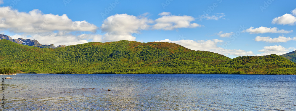 A hill behind a lake on summer day with clouds in the sky. Beautiful landscape view with greenery in