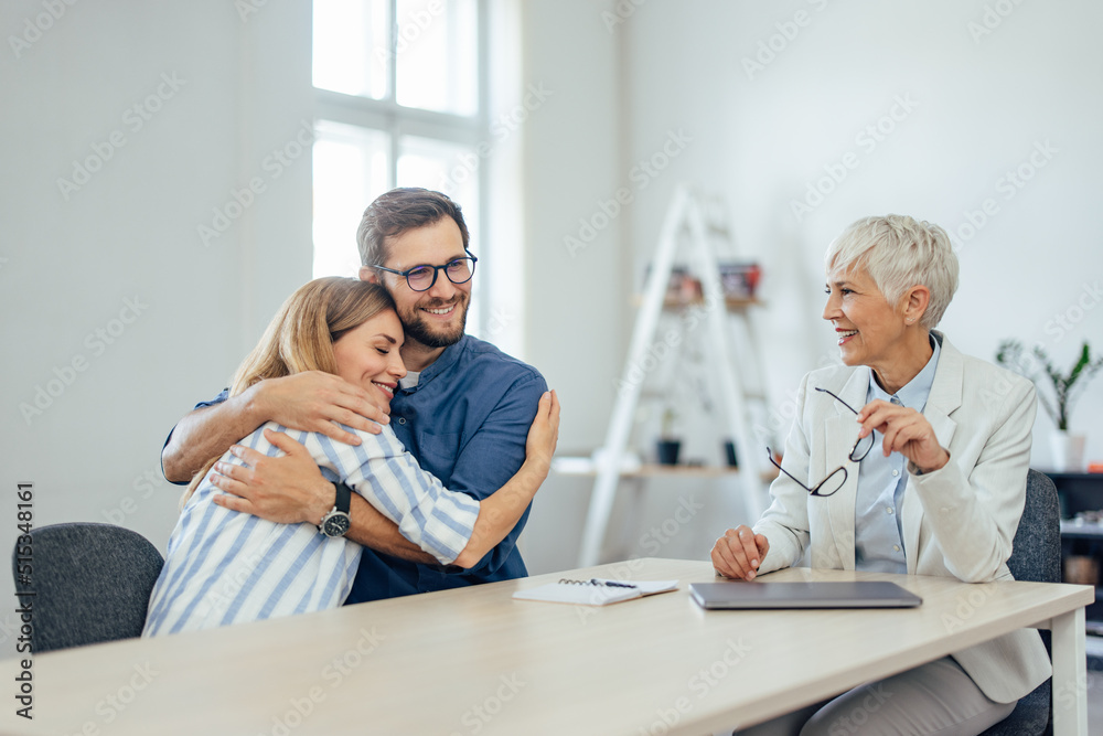 Woman and man at the insurance agents office, in a hug, insurance agent looking at them.