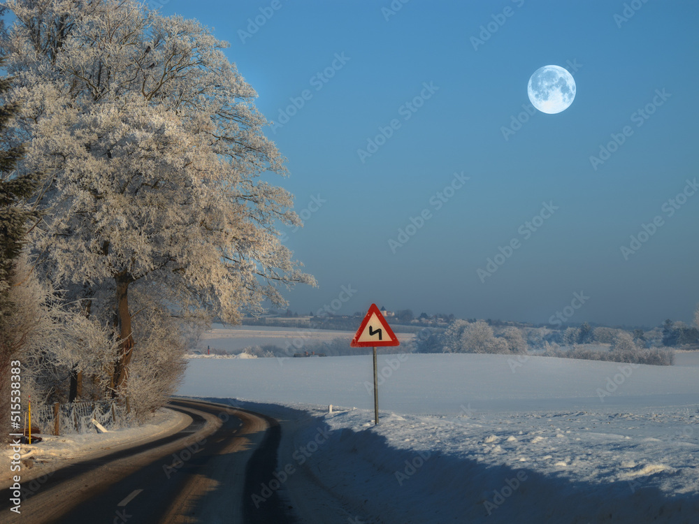 The winding road on a rural winter landscape with a sign on the side of the empty road for safety. A