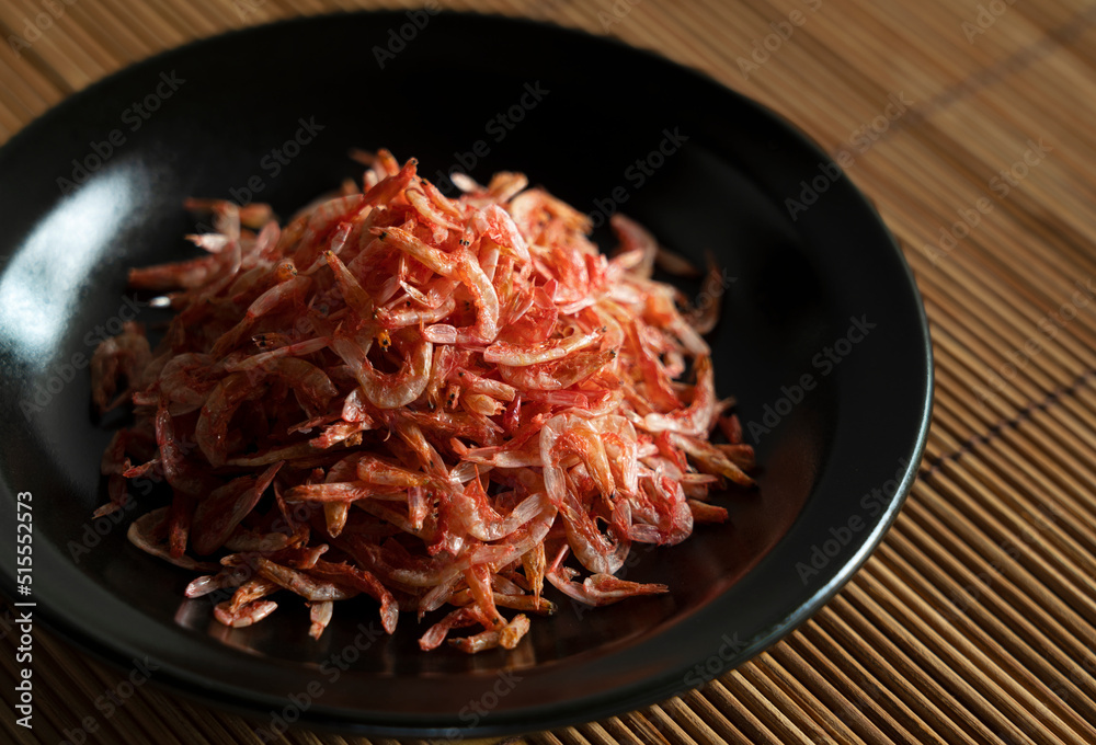 Dried sakura shrimps on a plate placed on a bamboo luncheon mat.