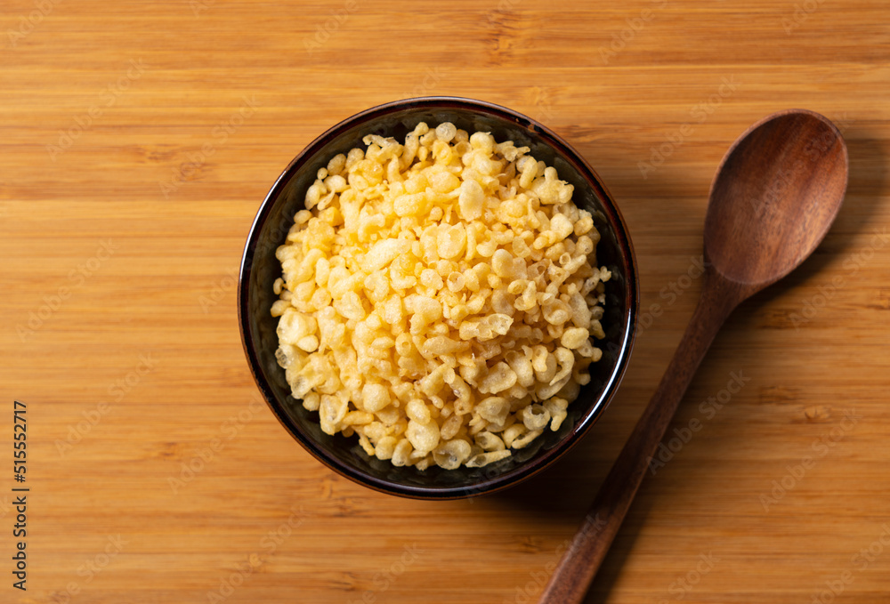 Tenkasu and wooden spoon served in a bowl placed on a wooden background.