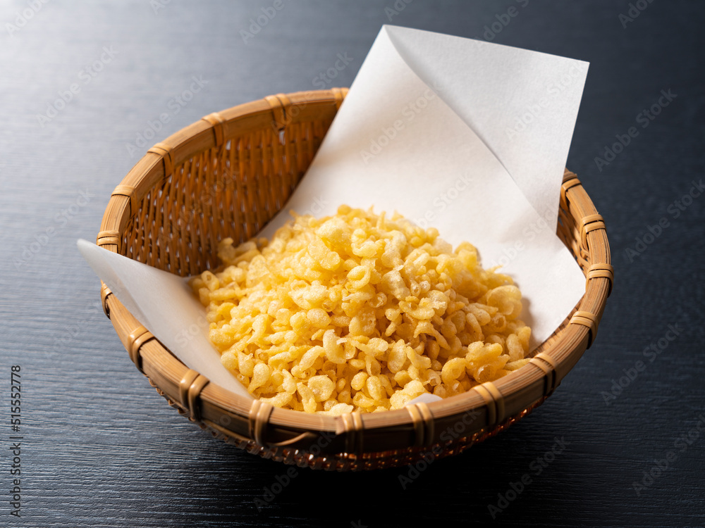 Tenkasu served in a colander placed on a black background.