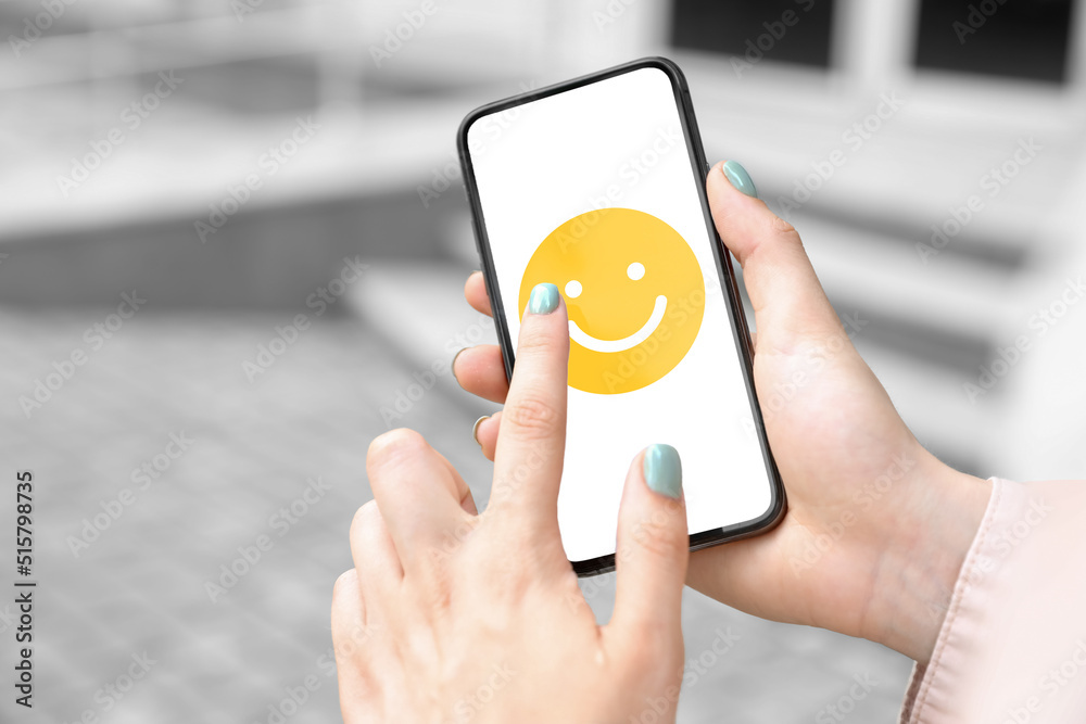 Woman holding phone with happy emoticon on screen outdoors, closeup