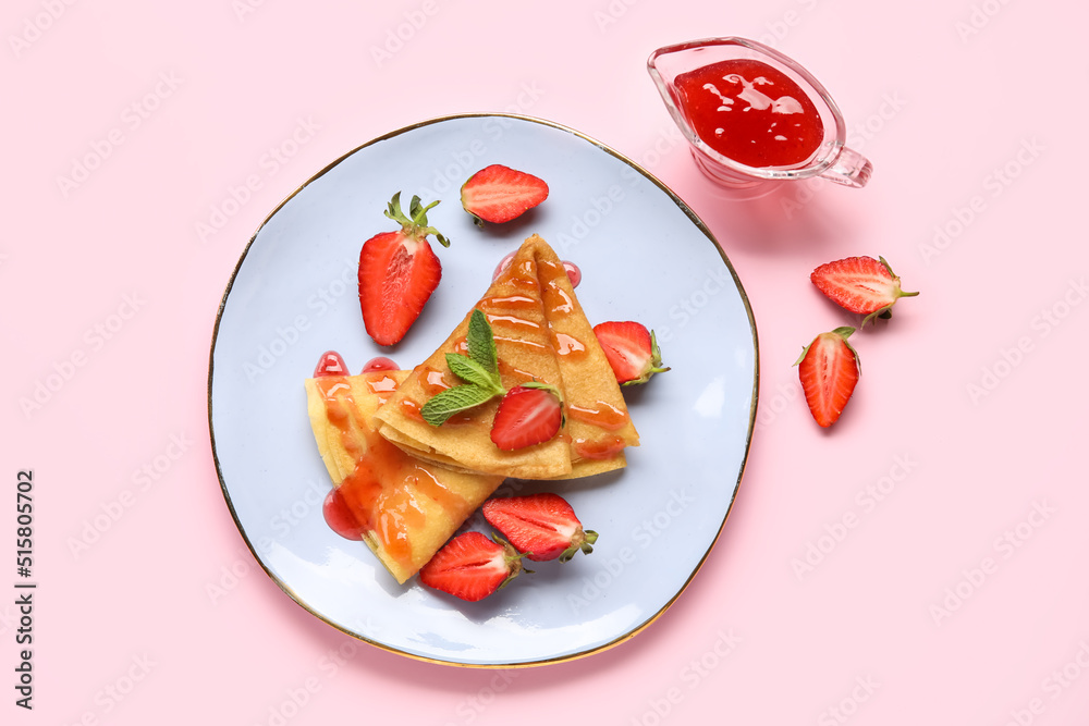 Plate of thin pancakes with strawberries, jam and mint leaves on pink background